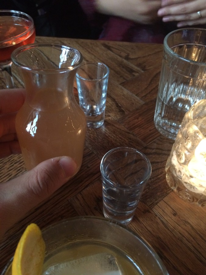 Small carafe of cloudy pink brine with two shot glasses in the background
