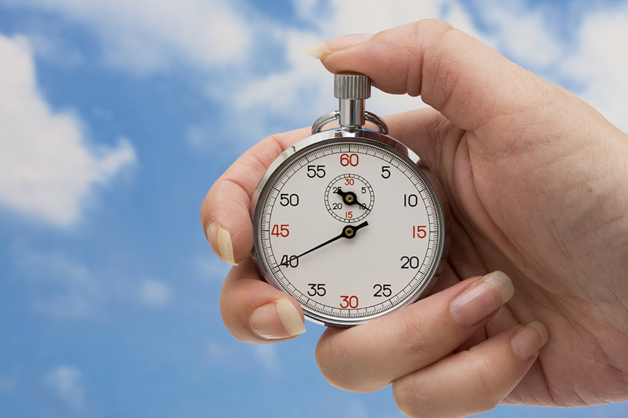 A hand holding a stopwatch against a background of a cloudy sky