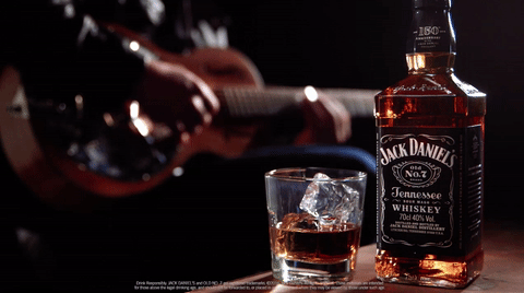 Animated Gif of a bottle and glass of Jack Daniels whiskey with some one playing guitar in shadow in the background