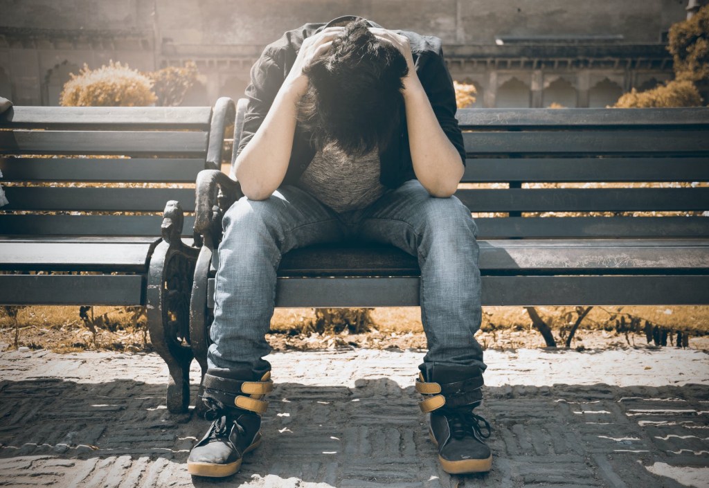 Young man on a park bench   Seated with his head in his hands, face down.