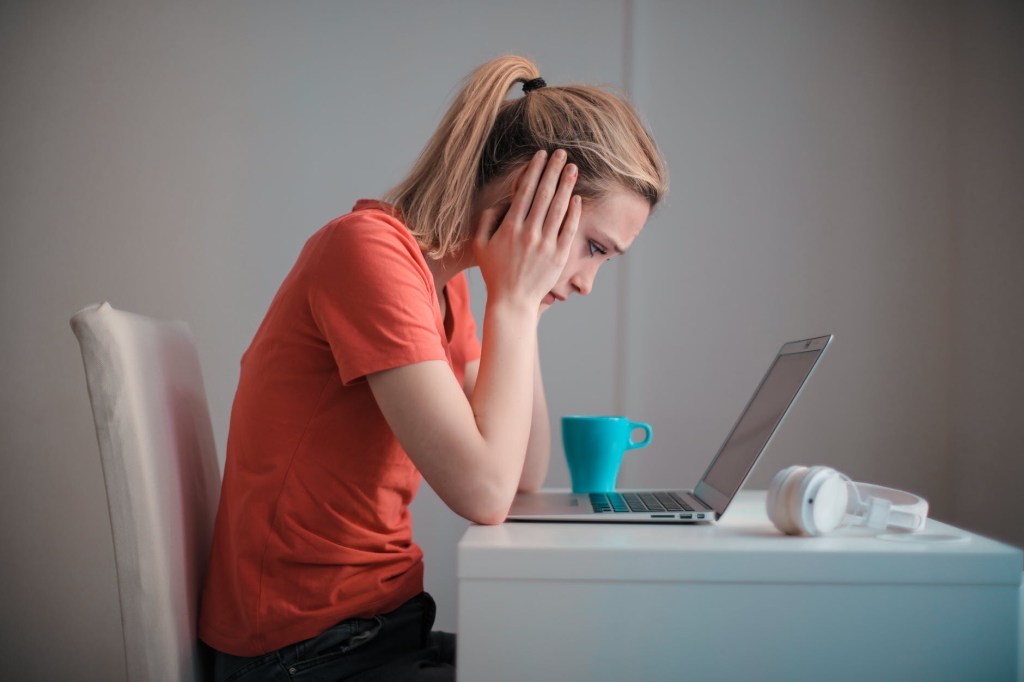 Young woman staring at her laptop in profile with her head in her hands