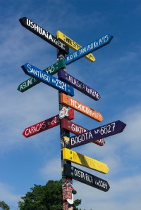 A multicolored sign post pointing to directions around the globe.