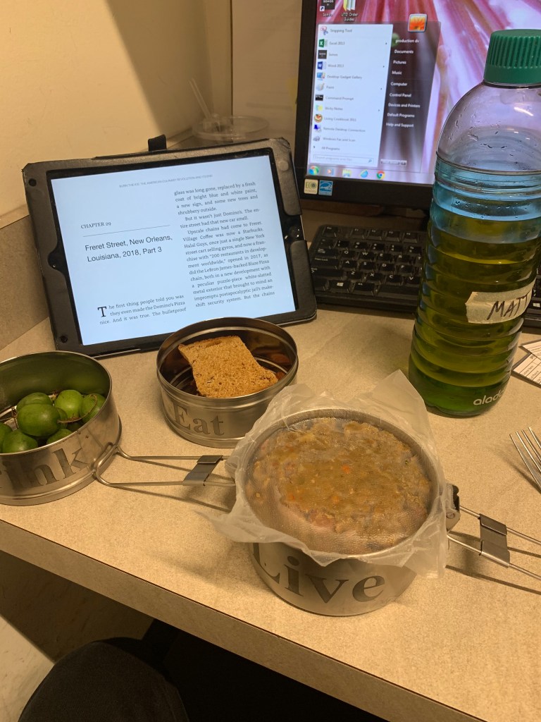 Lunch in tiffin containers, laid out on a computer desk with a bottle of water.