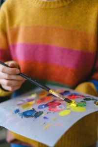 Picture of someone in a striped sweater mixing paints on an artist’s pallet.
