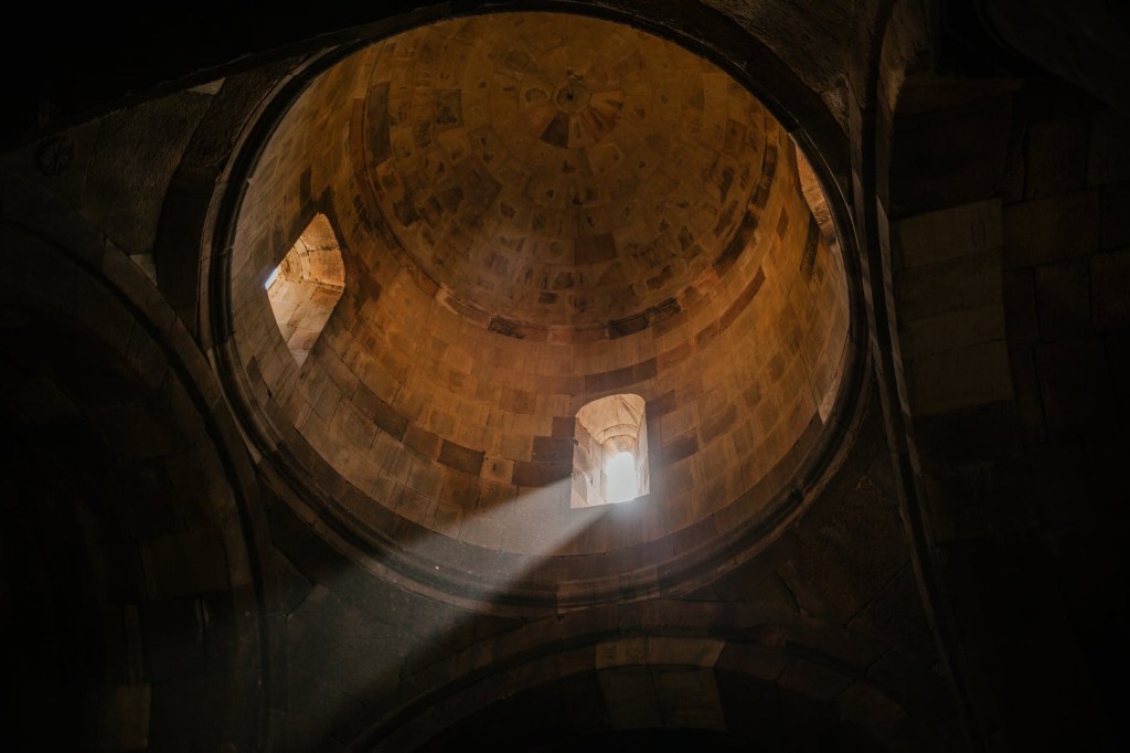 Light shines down through a small window in the dome of an otherwise darkened temple.