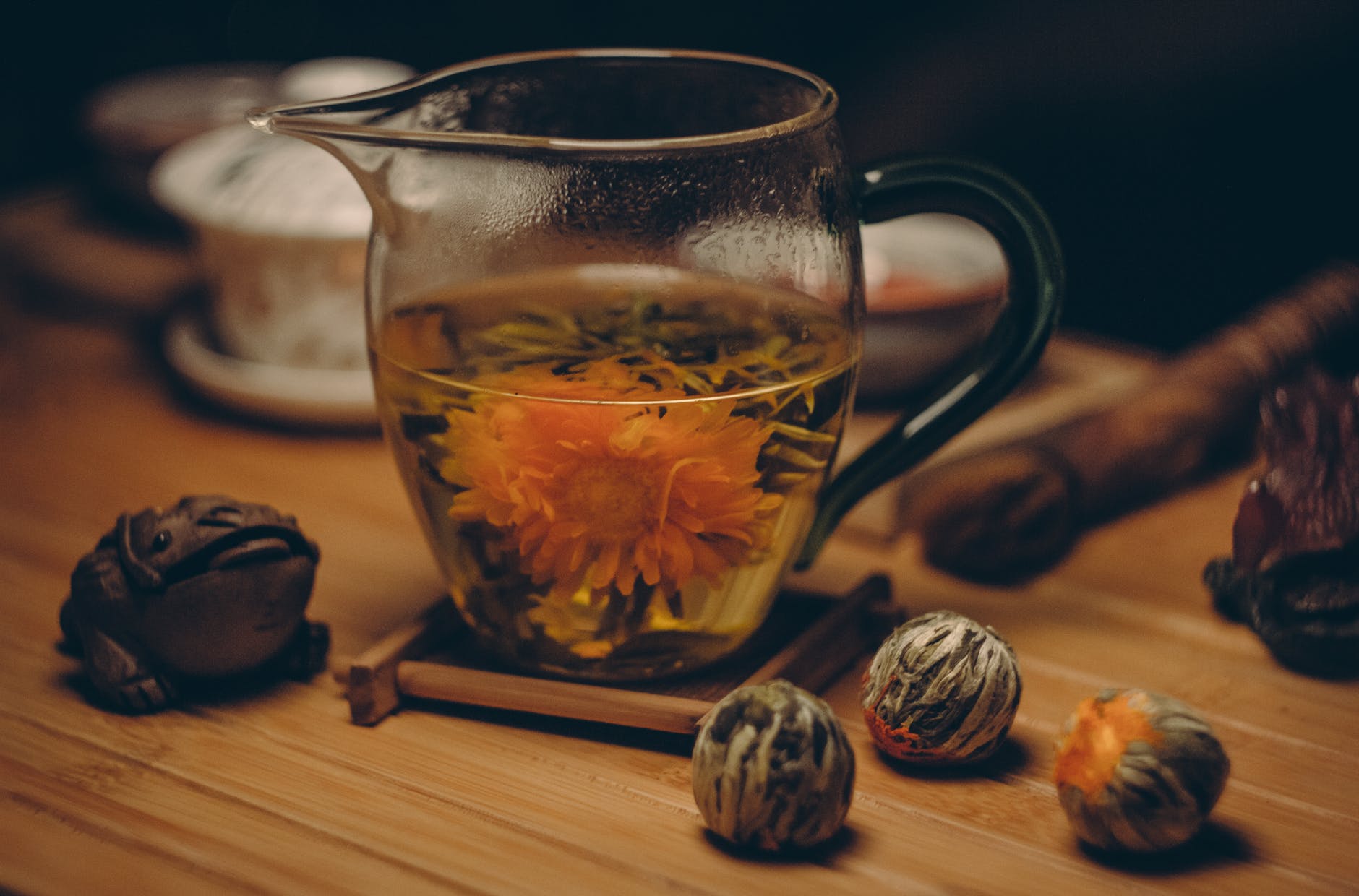 Close-up picture of blooming tea in a glass mug on a wooden table. Chinese tea paraphernalia is in the background.